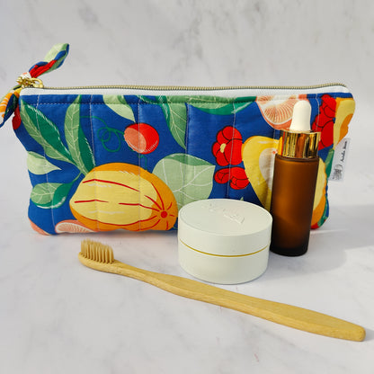Colorful floral-patterned pouch with a bamboo toothbrush, white container, and brown bottle on a light gray background