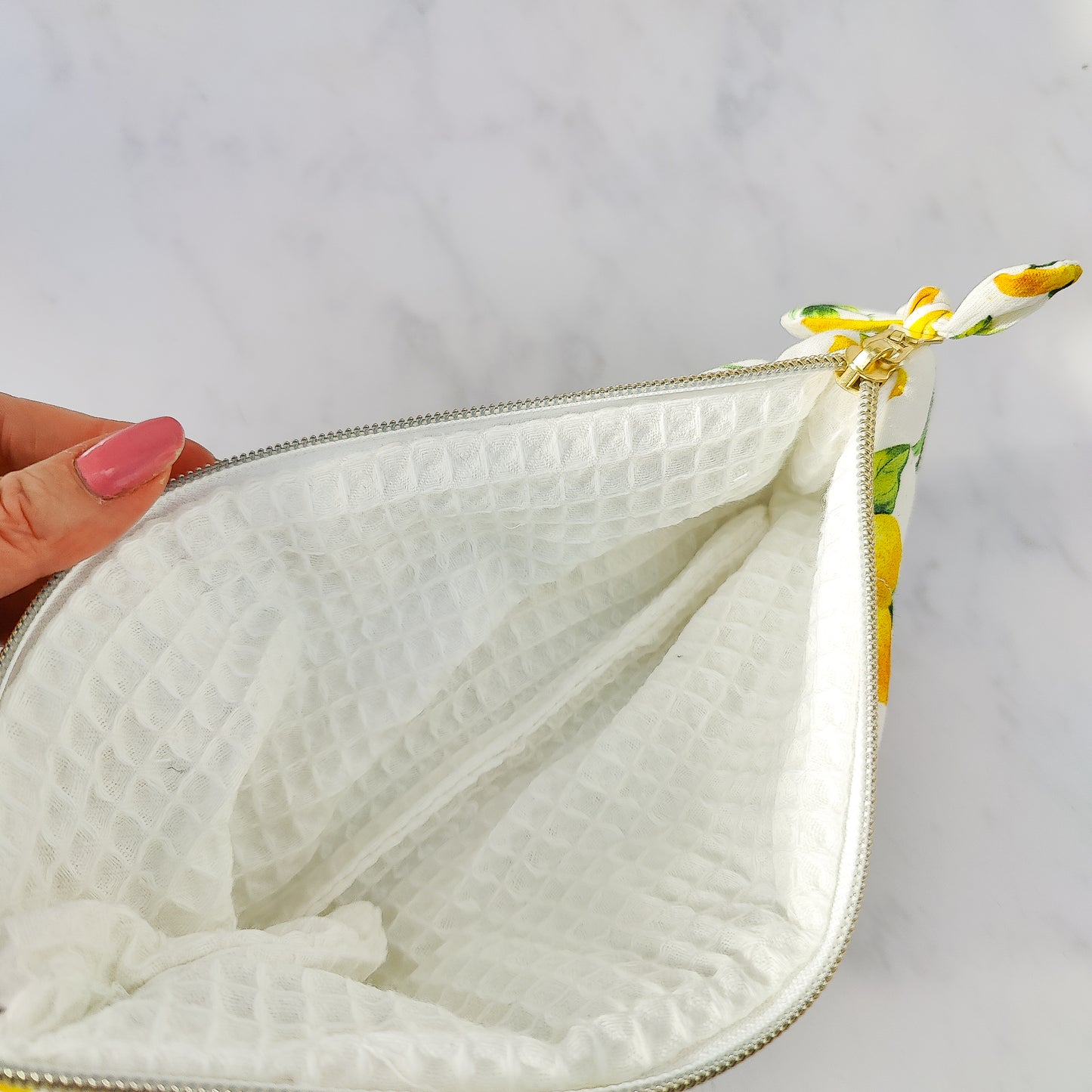 White textured pouch with a floral zipper pull held by a hand on a light gray background